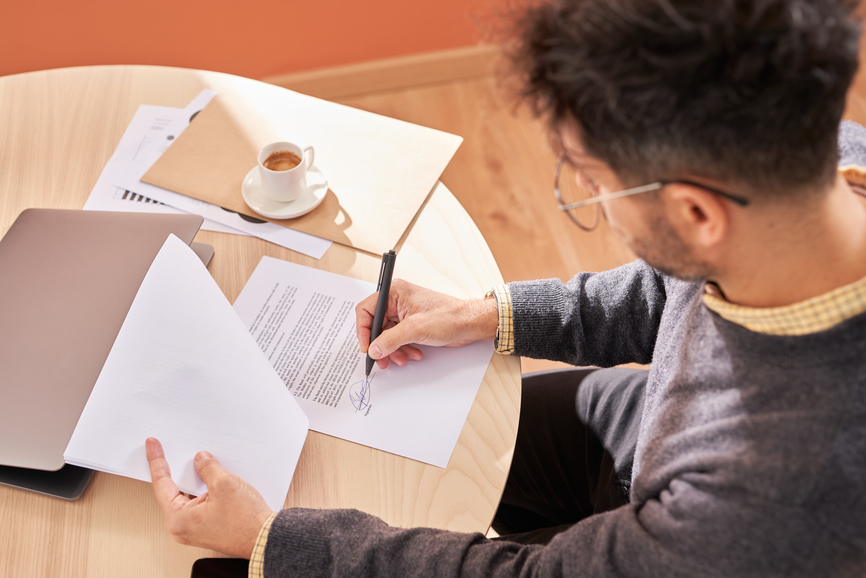 From above male employee writing signature on promissory note while sitting at table