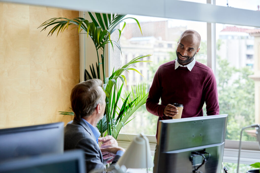 Two corporate co-workers having a conversation by the desktop in the office