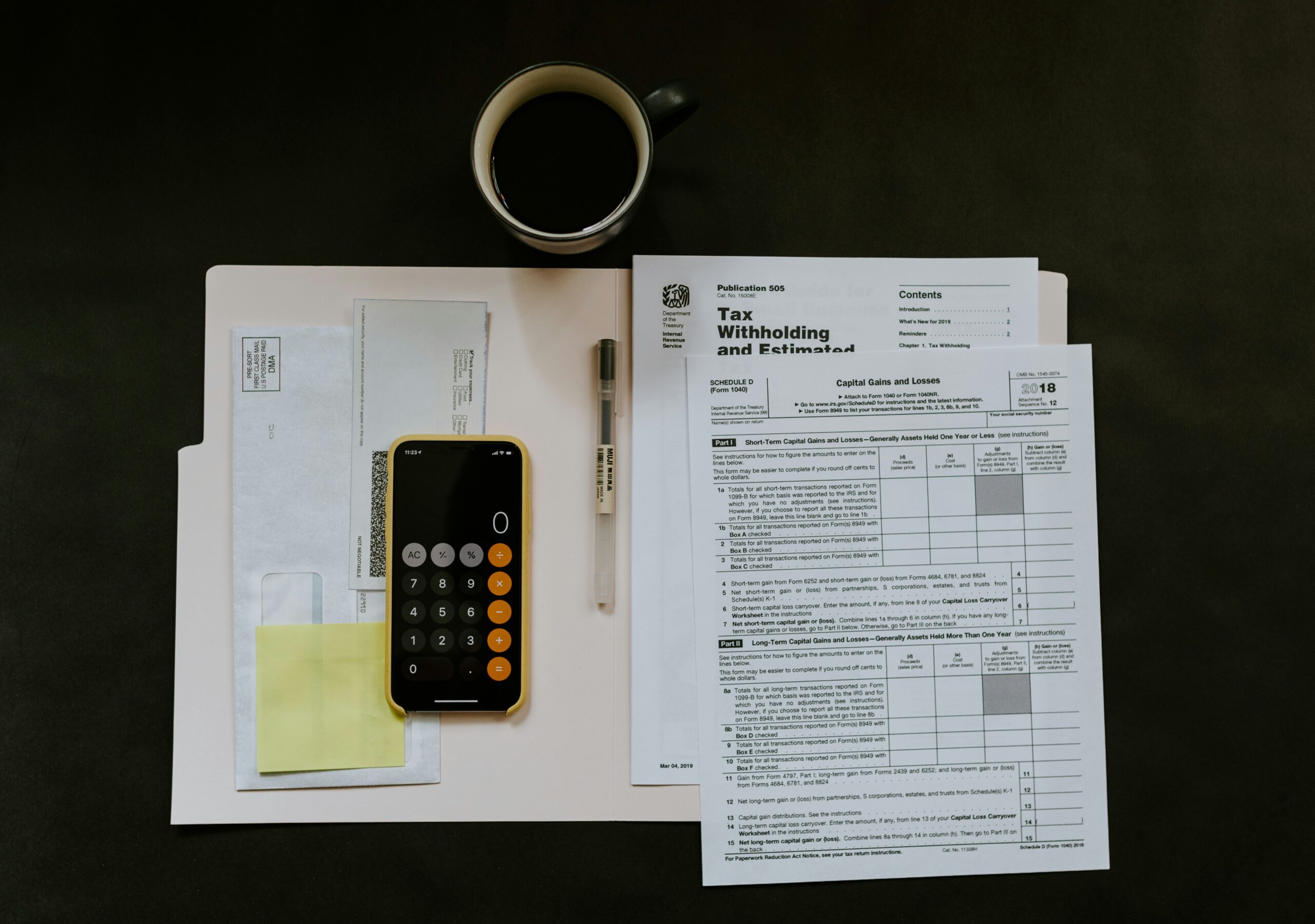 An open folder containing tax documents on a black backgroud, with a phone calculator and pen, alongside a fresh cup of coffee—ready to file taxes.