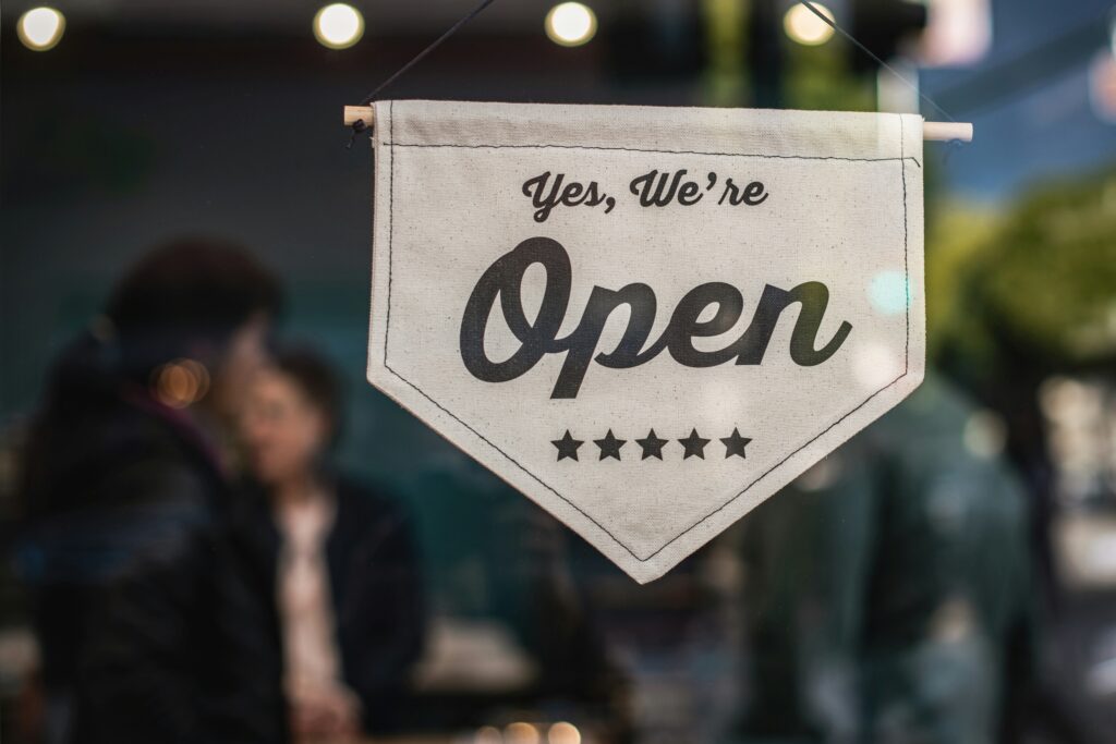 A cream colored sign on a blurry background that says "Yes, We're Open."
