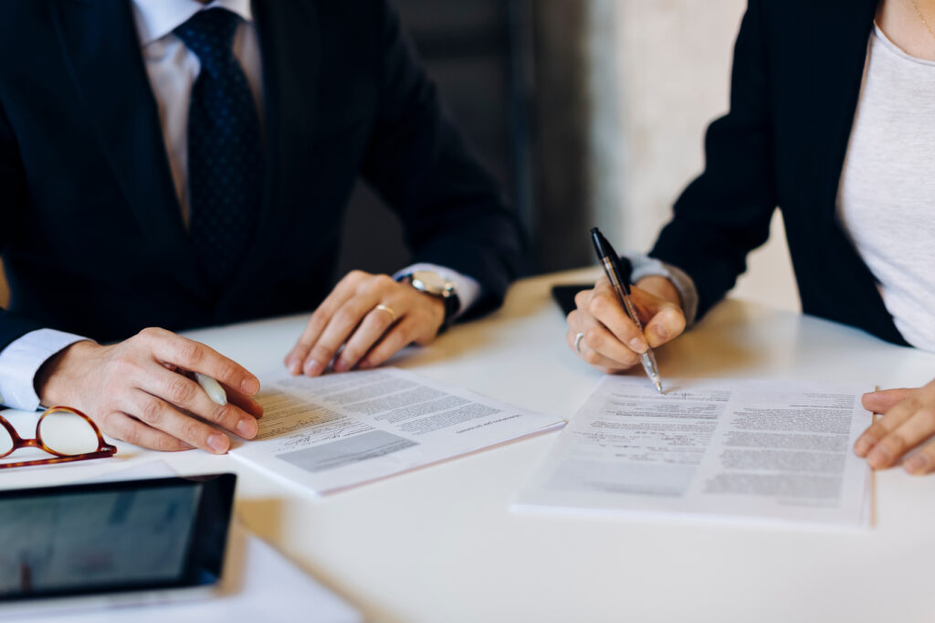 Crop business people sitting at table and signing papers during business meeting in contemporary office